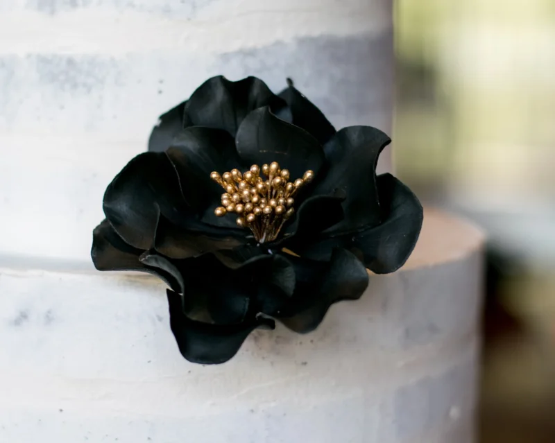 small black and gold open rose sugar flower on a buttercream cake